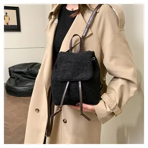 Détail d'un sac à dos en faux mouton noir avec lanières en cuir marron porté à l'épaule