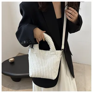 Close-up of white corduroy handbag with spiral handle and detachable fabric shoulder strap