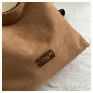 Detail of brown faux suede tote bag featuring a leather patch with gold lettering