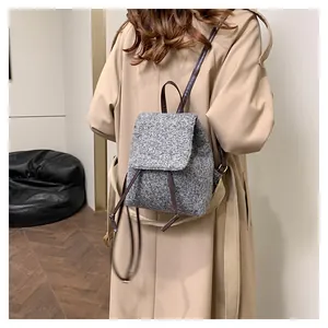 Détail d'un sac à dos en laine grise avec bretelles marron porté sur un trench-coat beige