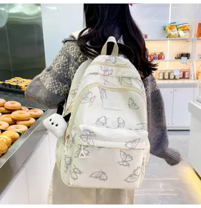 Detalle de mochila de lona blanca con estampado de mariposas y colgante de oso de peluche