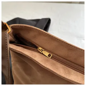 Detail of tan suede tote bag featuring a gold zipper closure and metal strap hardware