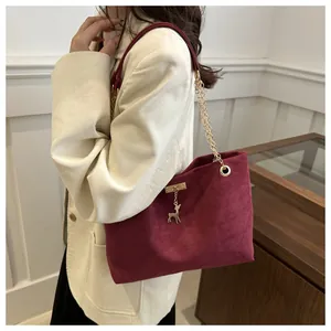 Détail du sac cabas en suédine bordeaux avec chaîne dorée et pendentif cerf sur un blazer