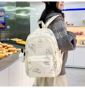 Detalle de la mochila de nailon crema impermeable con estampado de mariposas y peluche