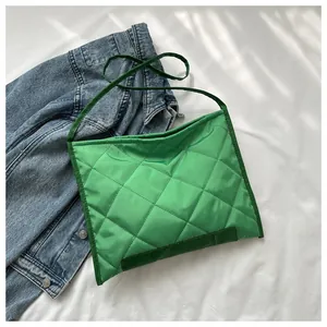 Close-up of green quilted shoulder bag with diamond pattern on white fabric