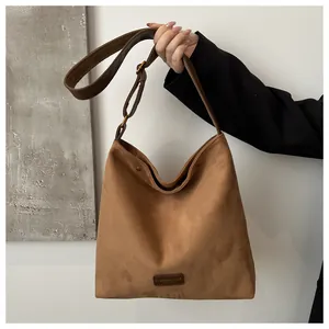 Detail of a brown suede hobo bag featuring a leather logo patch and metal buckle on the strap