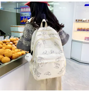 Detalle de mochila escolar beige con estampado de mariposas y colgante de peluche