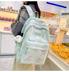Detalle de una mochila verde claro con estampado de mariposas y colgante de perro