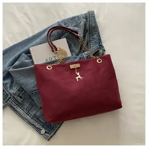 Détail d'un sac cabas bordeaux en daim avec bandoulière chaîne dorée et pendentif cerf