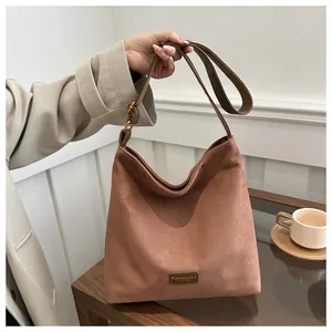 Detail of a brown suede hobo bag with leather label and bronze adjustable buckle strap