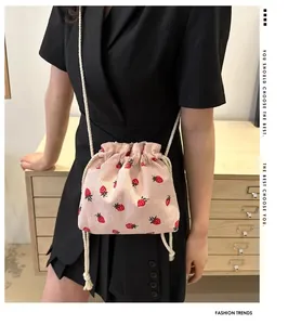 Detail of pink corduroy drawstring bag with red strawberry patterns and white woven strap