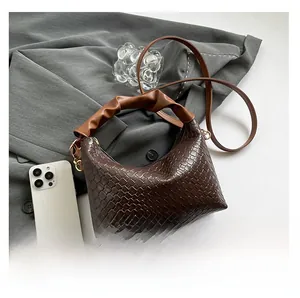 Detail of dark brown woven hobo bag with a light brown scrunchie handle on grey fabric