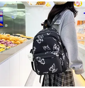 Detalle de mochila negra con estampados de mariposas blancas y un colgante de peluche