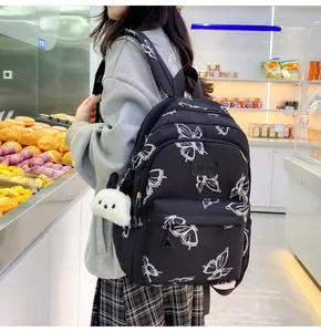 Primer plano de mochila negra con estampados de mariposas blancas y colgante de peluche
