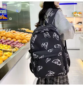 Detalle de mochila negra con estampados de mariposas y colgante de bola de pelo blanco