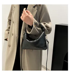 Detail shot of a black woven leather hobo bag worn with a beige wool coat in a luxury style
