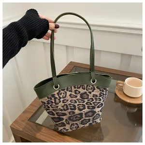Leopard print canvas tote bag with dark green leather straps in a home setting