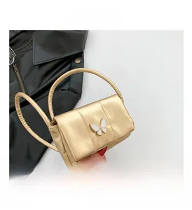Close-up of golden metallic mini bag featuring a decorative white butterfly clasp