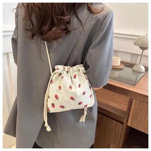Detail view of strawberry embroidered corduroy drawstring mini bucket bag with rope strap