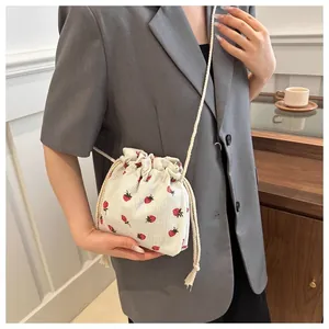 Detail shot of strawberry print corduroy bucket bag worn with a gray blazer