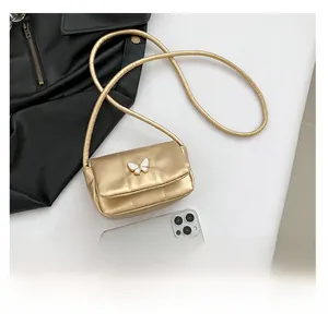 Golden mini crossbody bag with butterfly decor shown next to phone for size scale