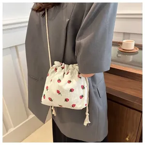 Close-up of beige corduroy drawstring bucket bag with strawberry print shown on model