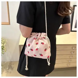 Detail of pink corduroy bucket bag with strawberry print and woven strap on model