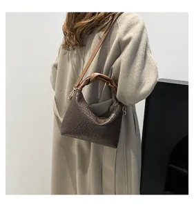 Detail of dark brown woven shoulder bag with knot handle and golden hardware on a beige coat