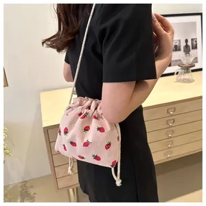 Detail view of pink corduroy mini bucket bag with embroidered strawberries and white rope strap