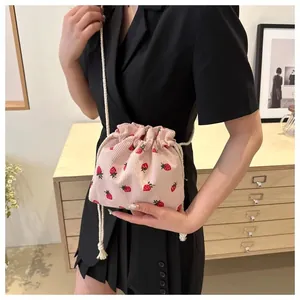 Side view of pink corduroy bucket bag with strawberry embroidery worn by a model