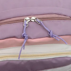 Detail of a dual metal zipper with purple cord pullers on a pastel patchwork backpack