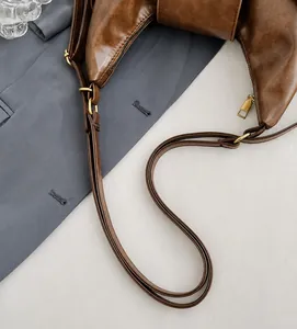 Detalle de la correa ajustable y hebilla de bronce en el bolso hobo de cuero PU marrón