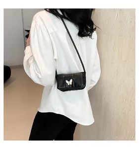 Detail of a black mini crossbody bag with a white butterfly buckle worn by a model