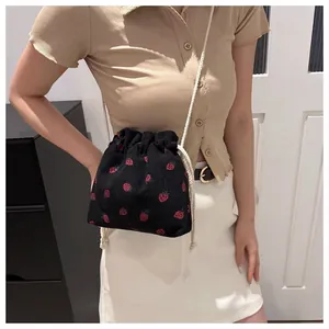 Detail view of black corduroy bucket bag with strawberry embroidery and rope straps