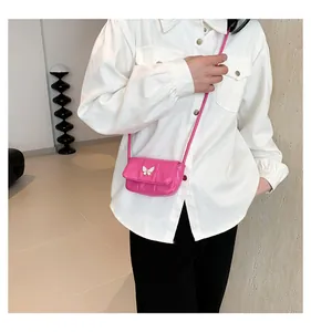 Mini magenta crossbody bag with a white butterfly buckle worn over a white shirt
