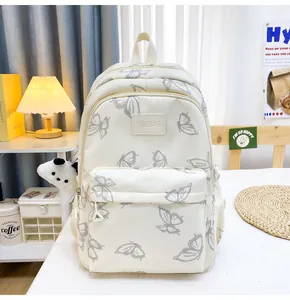 Detalle de la mochila crema con estampados de mariposas grises y un colgante de panda