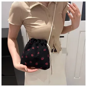 Close-up of strawberry print drawstring mini bag with cream woven shoulder strap