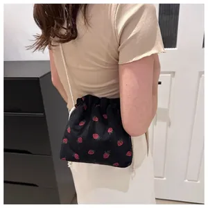 Detail view of mini black corduroy drawstring bag with red strawberry pattern on a model