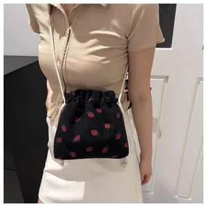 Detailed close-up of a black corduroy drawstring mini bag with red strawberry pattern
