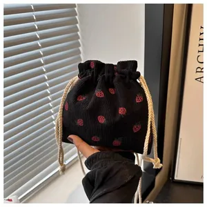 Close-up of black corduroy drawstring bag with vibrant red strawberry patterns