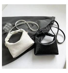 Close-up of woven shoulder bags in black and white with pleated handles and gold hardware