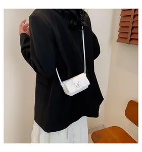 White mini crossbody bag with metal butterfly clasp shown on model in black blazer