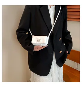 Detail of white quilted crossbody bag with golden butterfly buckle worn by model