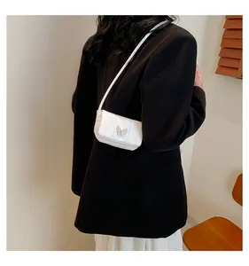 Detail of white mini crossbody bag featuring a silver butterfly buckle and glossy finish
