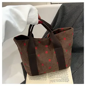 Handheld brown corduroy tote bag featuring red strawberry embroidery and dual straps