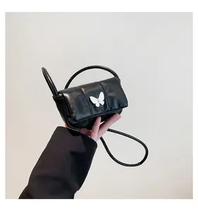 Detail of a black puffed crossbody bag with a white butterfly buckle held by a model