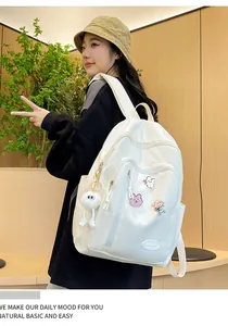 Détail d'un sac à dos en nylon blanc avec pins de dessin animé et pendentif en peluche