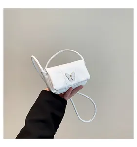 Detail of white leather mini bag featuring a decorative metal butterfly clasp and handle