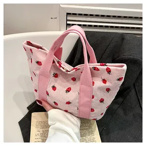 Close-up of pink corduroy tote bag featuring red strawberry patterns and sturdy woven handles