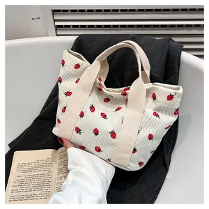 Detail of cream corduroy tote bag with strawberry prints on a gray suit jacket